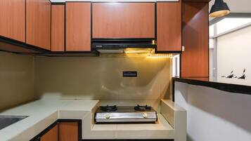 A compact kitchen with wooden cabinets, a stainless steel range, and a black pendant light.