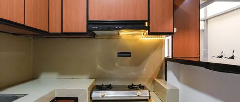 A compact kitchen with wooden cabinets, a stainless steel range, and a black pendant light.