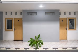 A room with two wooden doors, a large grey wall, and a potted plant. - INNCA Singa Utara, Semarang (Semarang)