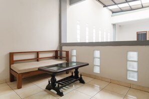 A room with a wooden bench, a glass-top table, and a view of a building through a window with blinds. - INNCA Singa Utara, Semarang (Semarang)