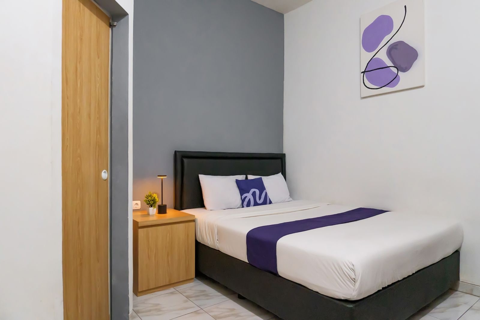 A bedroom with a bed, bedside table, lamp, and a wall art piece.