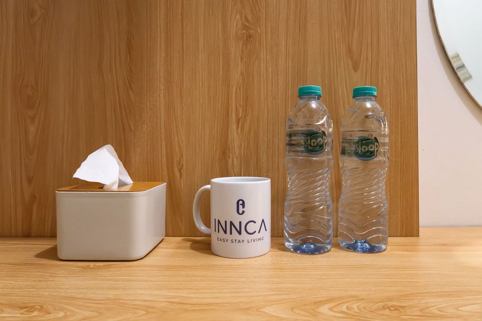 A tissue box, a mug with 'INNCA' branding, and two water bottles on a wooden surface.