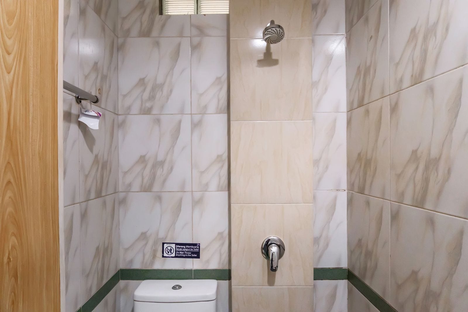 A bathroom with marble tiles, a toilet, a showerhead, and a sign indicating no flushing.