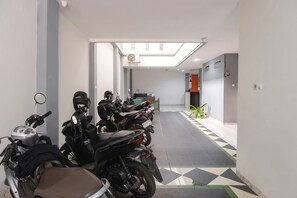 A hallway with multiple motorcycles parked, a ceiling fan, and a plant. - INNCA Singa Utara, Semarang (Semarang)