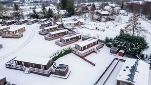 Estância coberta de neve com várias cabanas e um edifício central, em meio a uma paisagem nevada e montanhas.