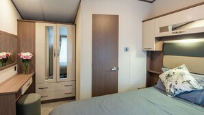Quarto com cama, guarda-roupa, espelho e secretária com um vaso de flores.