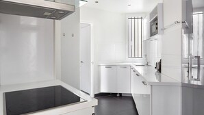Une cuisine moderne avec des meubles blancs, un pare-feu en verre et une plaque de cuisson noire.