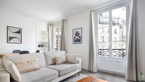 Un salon moderne avec un canapé, une table basse et de grandes fenêtres dotées de rideaux.