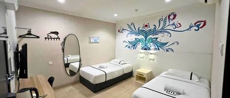 Habitación de hotel con dos camas, un escritorio con hervidor, un espejo y un calentador de pared.