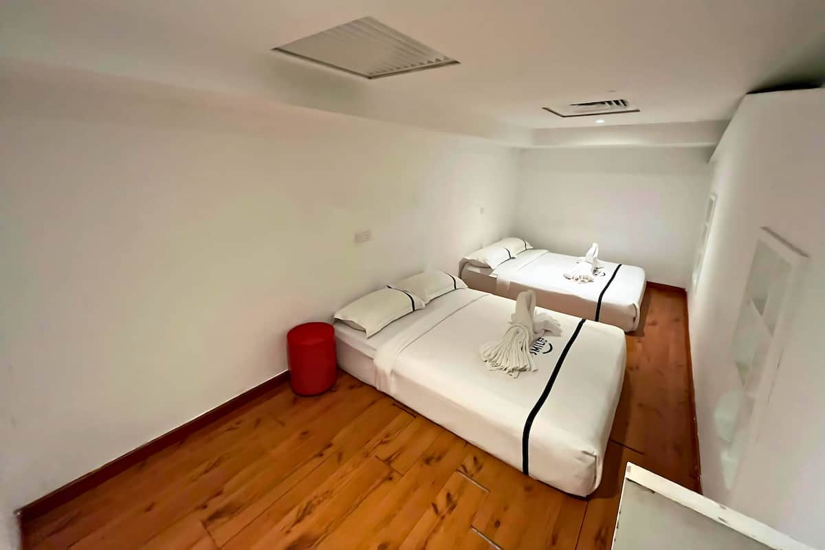 A small, compact room with two single beds, a red trash bin, and a wooden floor.