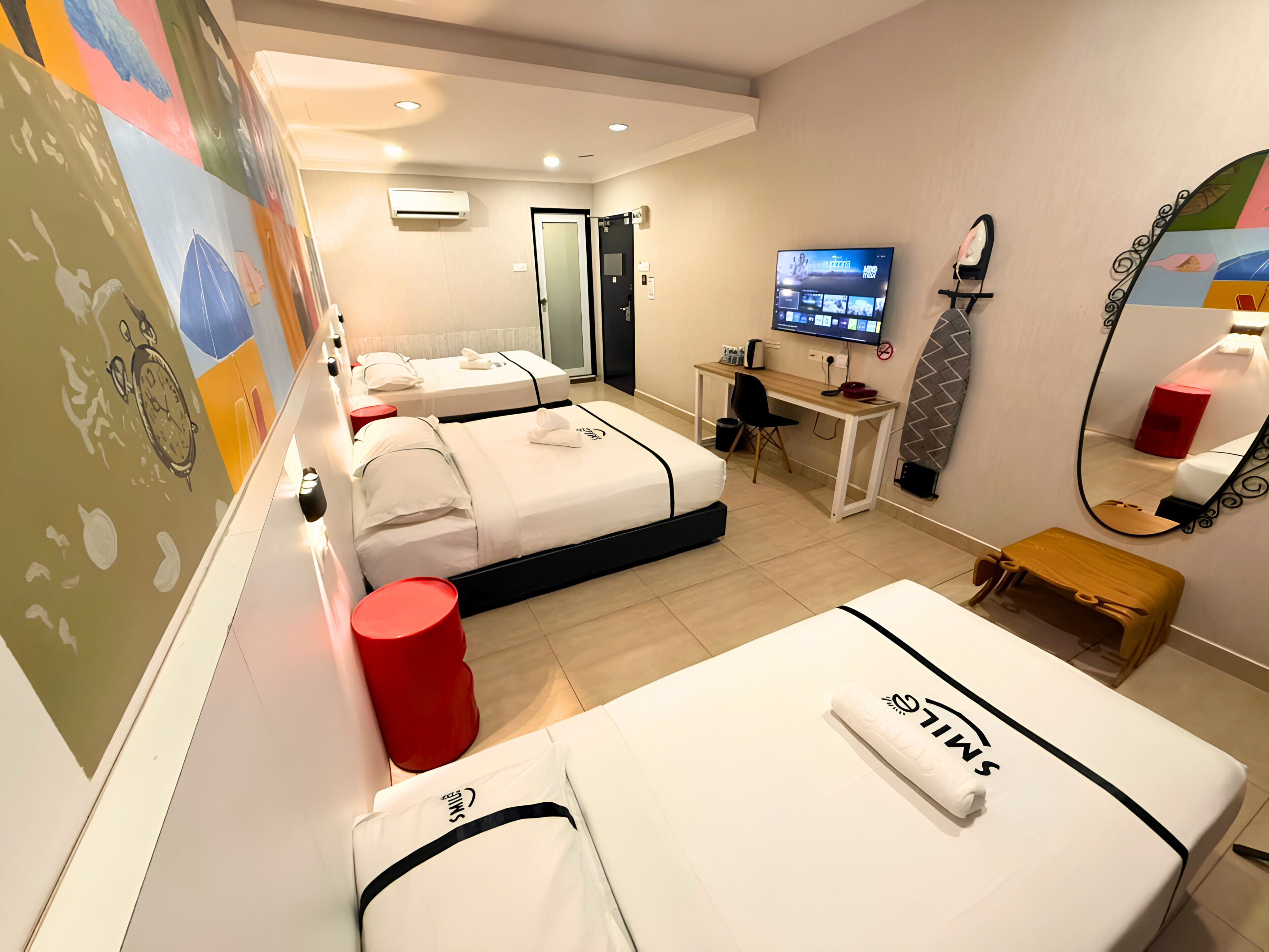 A hotel room with two beds, a desk, a TV, a mirror, and a red trash bin.