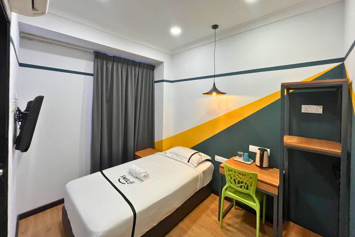 A compact hotel room with a single bed, a desk, a chair, and a small table.