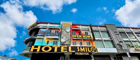 A hotel with a modern facade, multiple balconies, and a prominent 'OPEN NOW' sign.