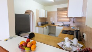 A compact kitchen with a refrigerator, microwave, sink, and a small dining area with a table set for two. - Coastal Comfort | Balcony | Pool | Sea Views (Margate)