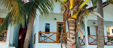 A beachfront property with a white building, palm trees, and a sandy ground.