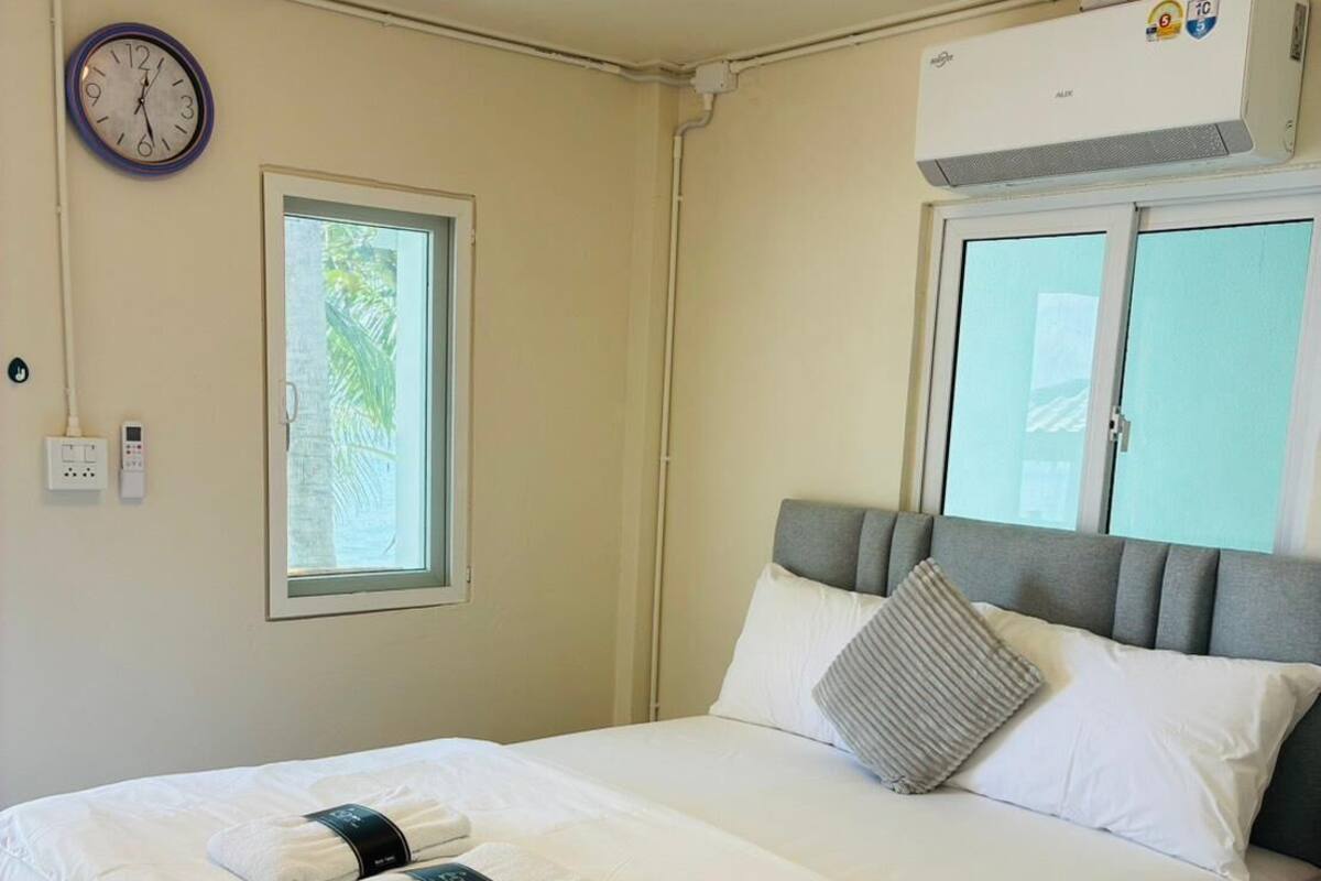 Ein ordentlich bezogenes Bett mit weißen Leinen und zwei Handtüchern, ein grauer Kopfteil sowie ein Fenster mit Blick ins Grüne.