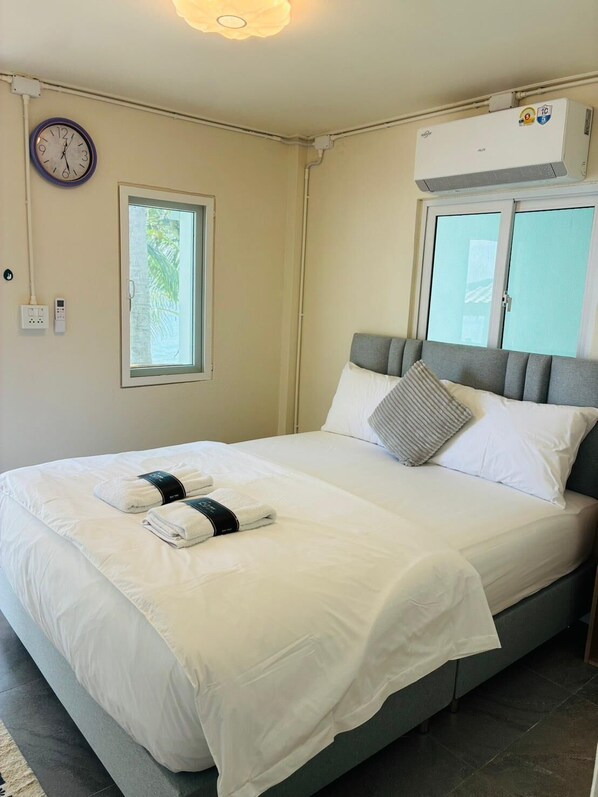 A neatly made bed with white linens and two towels, a grey headboard, and a window with a view of greenery. - Lamai Beachnest Bunaglows (Koh Samui)