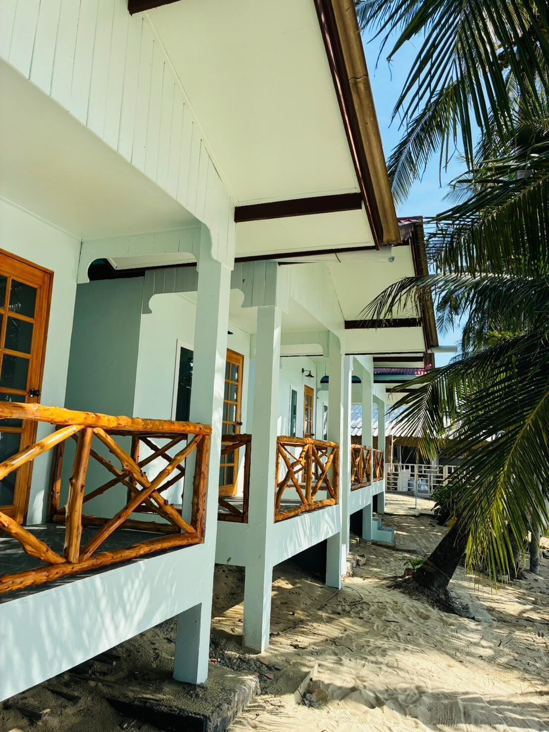A beachfront hotel with multiple rooms, each featuring a wooden balcony and a view of the sandy beach.