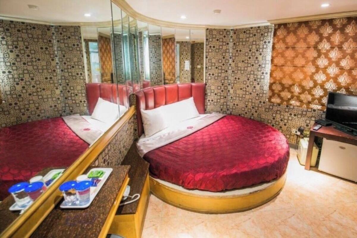A hotel room with two beds, a television, a minibar, and a mirror.