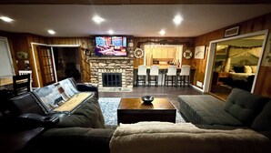 Een gezellige woonkamer met een stenen open haard, een televisie en een eethoek met barstoelen.