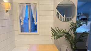 Ein Essbereich mit Holztisch und Stühlen, einem fenster mit Vorhängen, einer Topfpflanze und einem runden Spiegel an der Wand.
