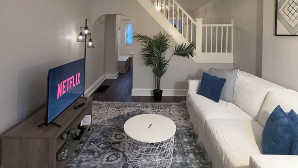 Ein Wohnzimmer mit einem weißen Sofa, einem Couchtisch, einem Fernseher und einer Treppe zu einem anderen Raum.