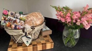 Una bandeja de madera con una cesta que contiene diversos objetos, incluyendo un florero con flores rosadas.