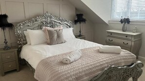 Un dormitorio con una cama grande, un cabecero decorado, dos mesitas de noche, un aparador y una araña.