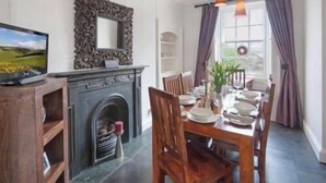 Un comedor con chimenea, sillas de madera, una mesa dispuesta para cuatro personas y vistas amplias a través de grandes ventanales.