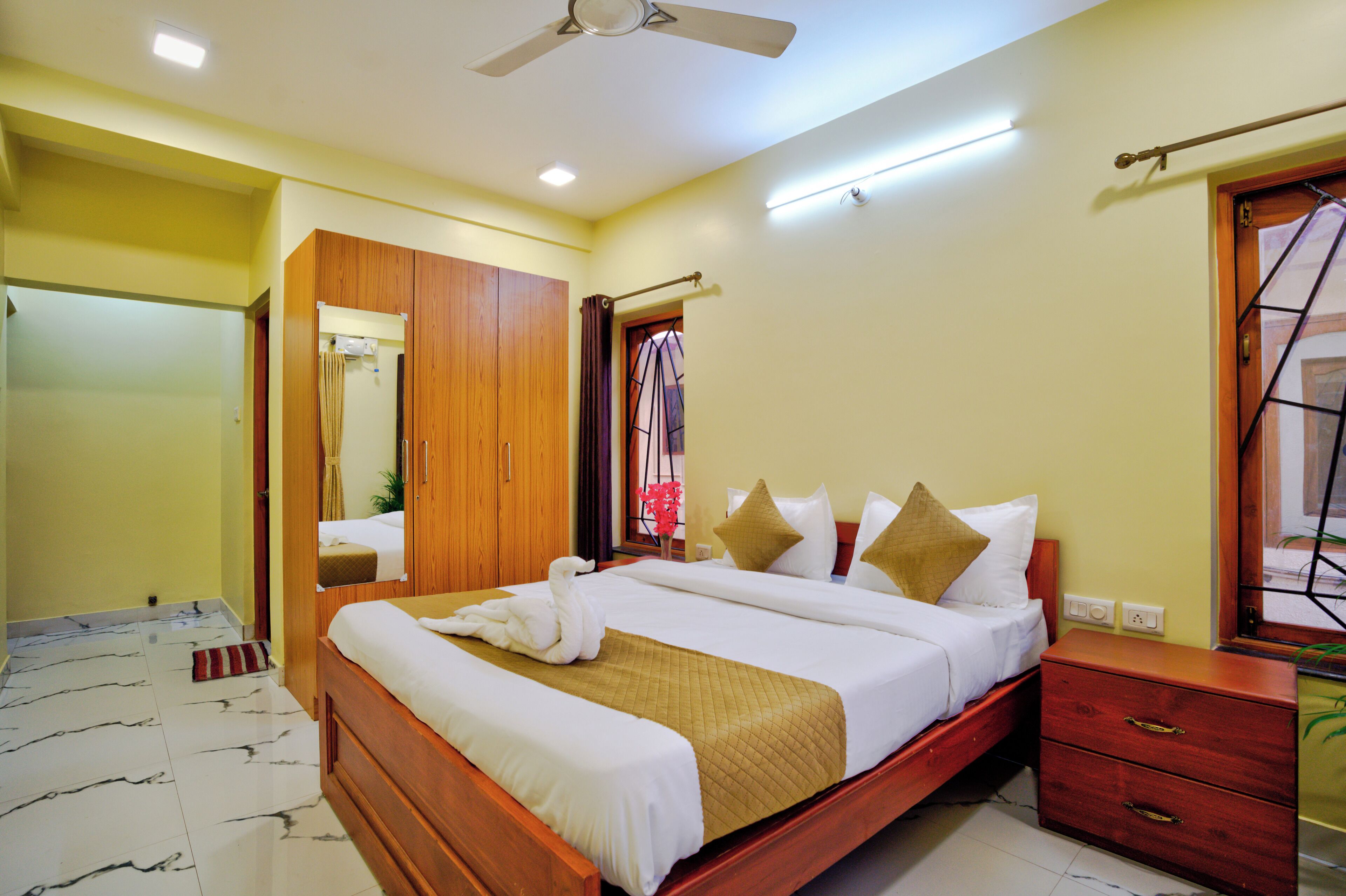 A hotel room with a bed, wooden wardrobe, and a ceiling fan.