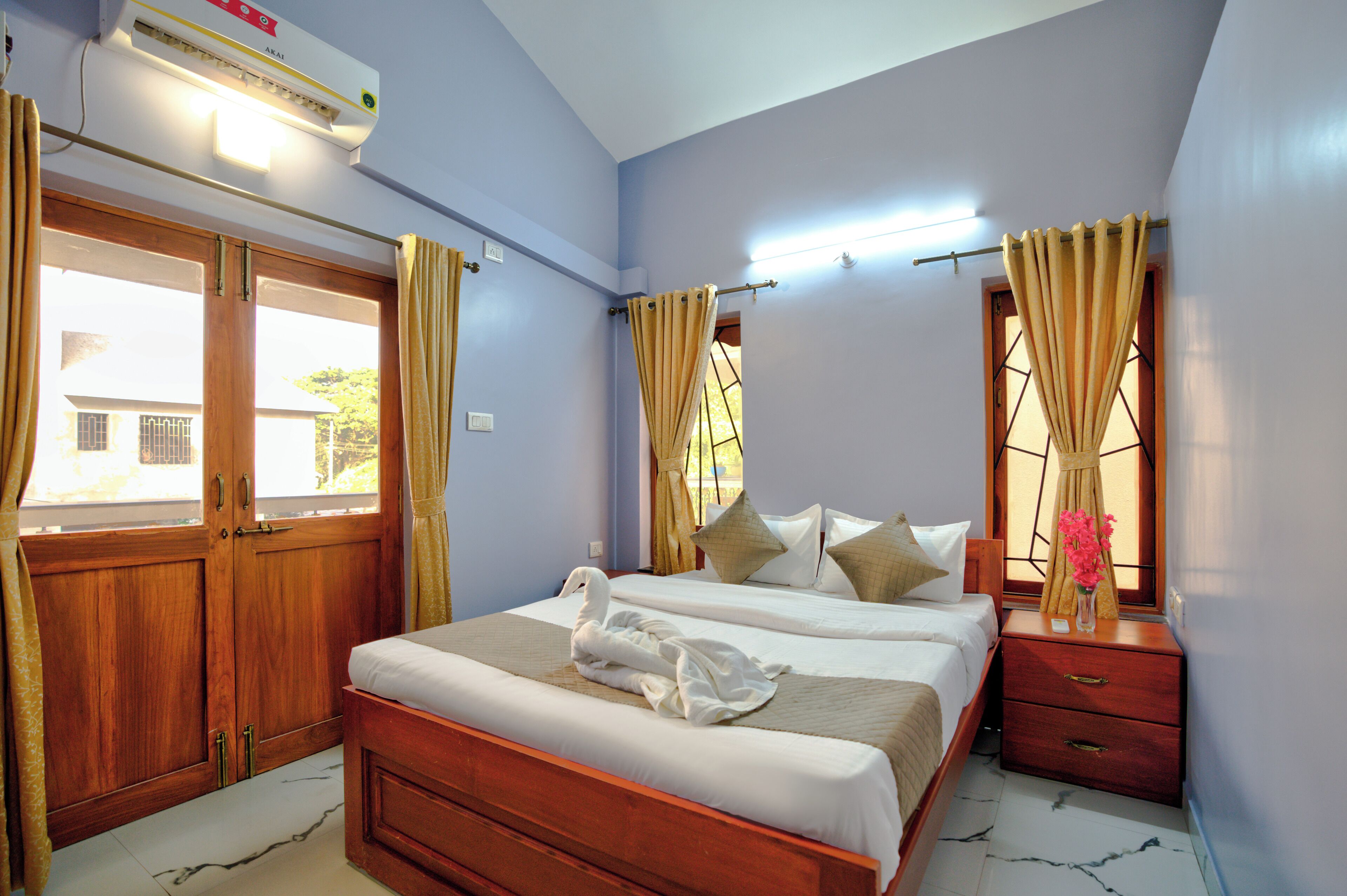 A bedroom with two beds, wooden wardrobe, and a nightstand with a vase of flowers.