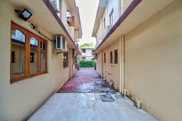A narrow alleyway between buildings with tiled flooring, air conditioning units, and a small gate at the end. - Eyokar 4 BHK Villa Candolim (Nerul)