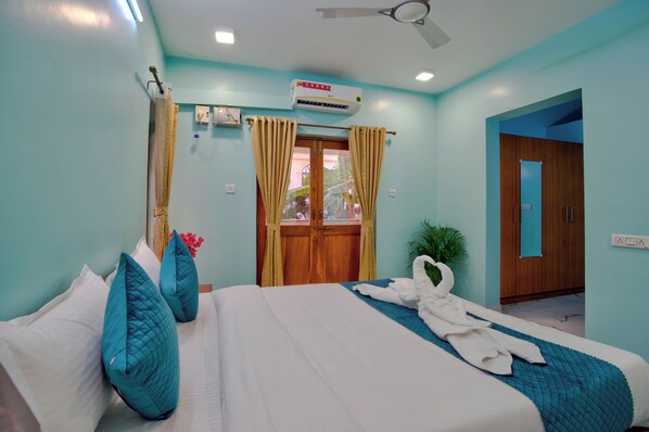 A hotel room with a bed, curtains, a ceiling fan, an air conditioner, and a wooden door.