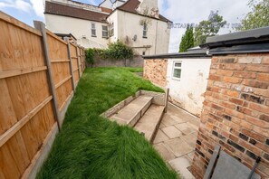 A narrow backyard with a wooden fence, a grassy area, and a brick wall. - Cosy Studio in great location near the City (Birmingham)