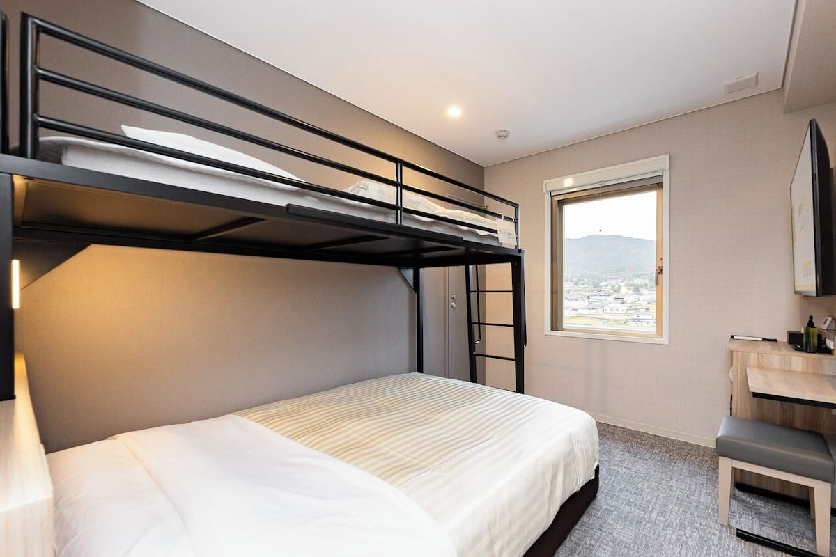 Habitación de hotel con literas, un escritorio con silla, un ventanal con vista a la ciudad y un televisor montado.