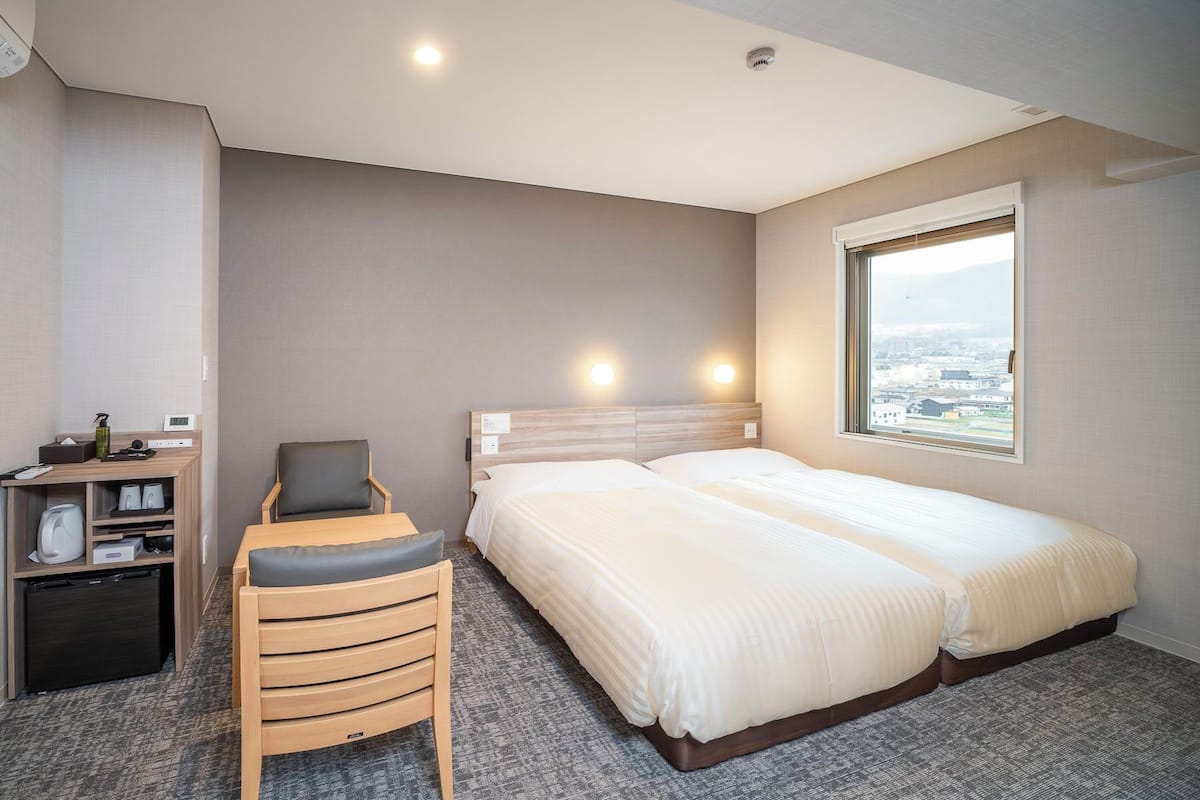 Habitación de hotel con cama, escritorio con silla, una mesita y ventana con vista a la ciudad.