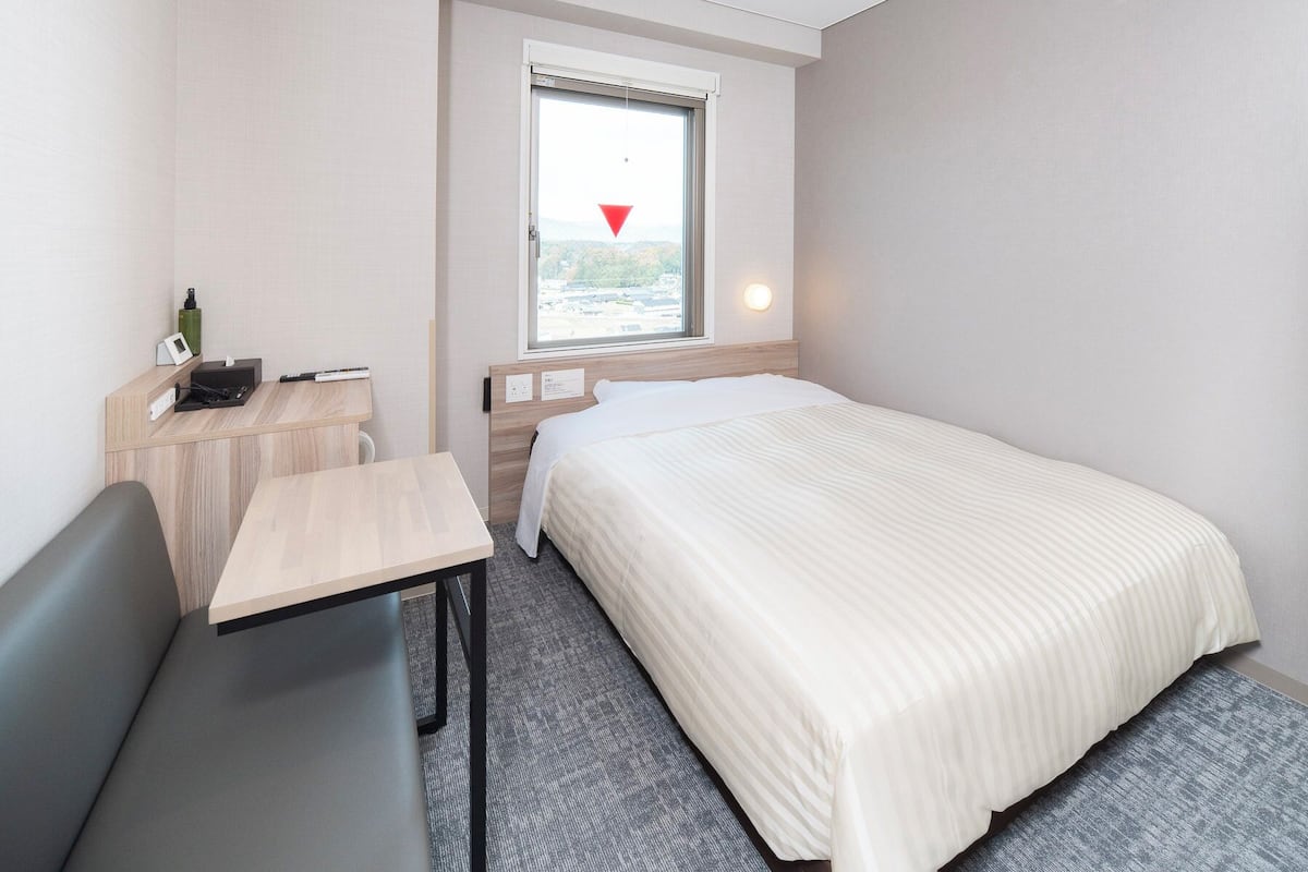 Habitación de hotel con cama, escritorio, silla, ventana con vistas y aire acondicionado instalado en la pared.