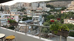 A balcony with potted plants and a table, overlooking a densely packed urban area with various buildings and a hillside in the background. - Albania Dream Saranda Apartments (Saranda)