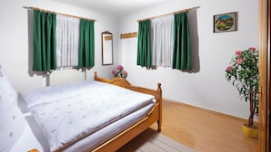 Un dormitorio con una cama de madera, cortinas verdes y blancas, una planta en maceta y un cuadro en la pared.