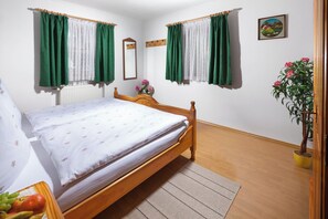 A bedroom with a wooden bed, green and white curtains, a potted plant, and a painting on the wall. - Vacation apartment Watzmann for 2 - 3 persons, 42sqm, 1 bedroom, south-facing balcony (Schönau am Königssee)