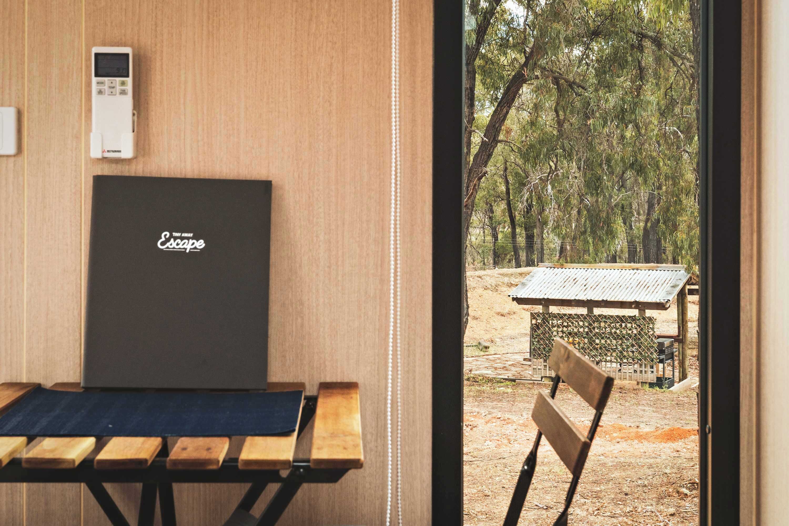 A room with a wooden table, a black laptop, and a view of a forest through a window.