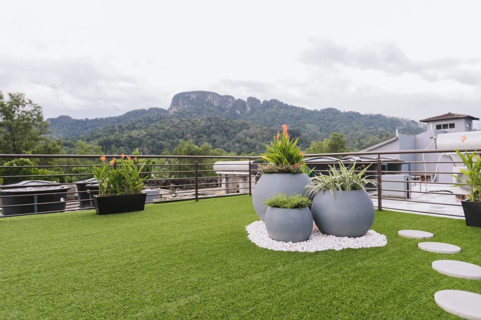 A rooftop garden with artificial grass, large grey planters with plants, and a mountainous backdrop.