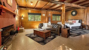 A log cabin interior with a fireplace, leather sofa, wooden coffee table, and a bed with a headboard.