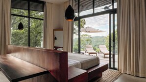 Un dormitorio con una cama grande, un banco de madera, un escritorio y vistas a un balcón con sillas y una mesa.