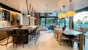 Una cocina moderna con una isla central, asientos tipo barra y un comedor con una mesa grande y sillas.