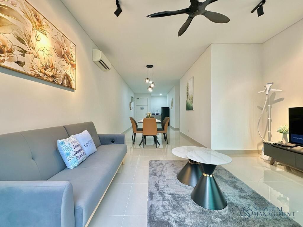 A modern living room with a grey sofa, a round coffee table, and a dining area in the background.