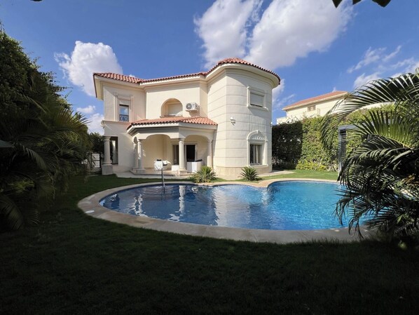 Ein zweistöckiges Haus mit Swimmingpool, umgeben von viel Grün.