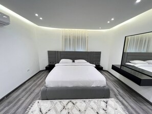 Une chambre à coucher moderne avec un grand lit, des tables de chevet, un miroir et un luminaire au plafond.