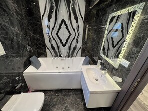 Ein Badezimmer mit Marmorwand, einer Badewanne, einem Waschbecken und einer Toilette.