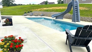 A swimming pool with a slide, outdoor seating, and a potted plant.